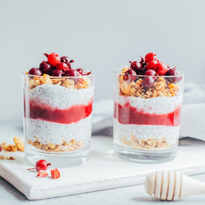 Chia parfaits layered with granola and berry puree in glass cups beside a milk bottle.
