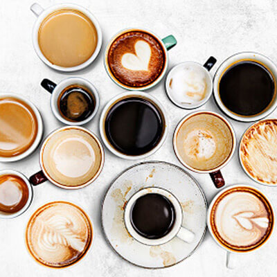 Assorted cups of coffee with various colors and latte art arranged on a light surface.
