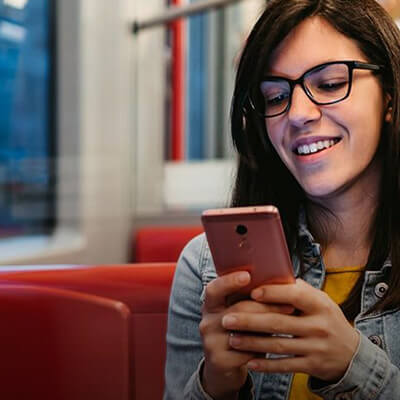 Person sitting on public transit using a smartphone while seated among red and yellow interior poles and seats.