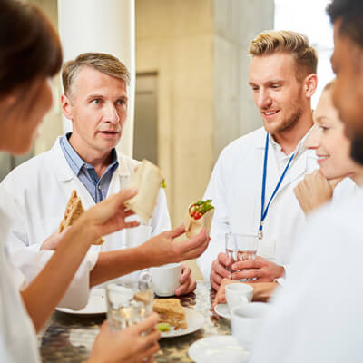 Healthcare professionals in lab coats sharing food and drinks during a casual break.