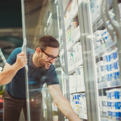 Person opening a refrigerated glass door and selecting a dairy product from a well-stocked cooler in a grocery or convenience store.