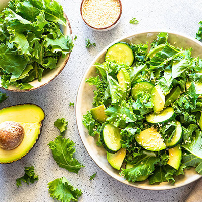 Fresh green salad with kale, avocado slices, and cucumbers in a bowl on a kitchen counter.