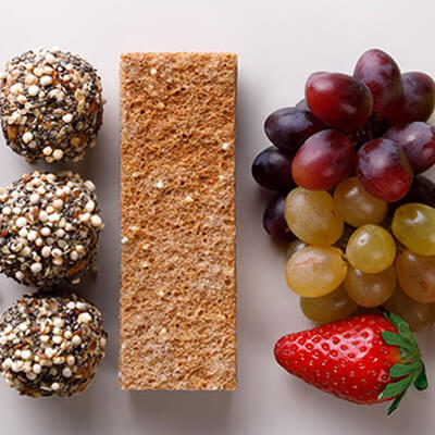 Assorted healthy snacks including veggies, nuts, energy bites, a granola bar, grapes, and a strawberry.