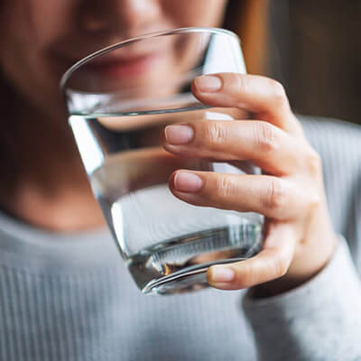 Close-up of a person holding a clear glass of water with one hand, wearing a light gray ribbed shirt.