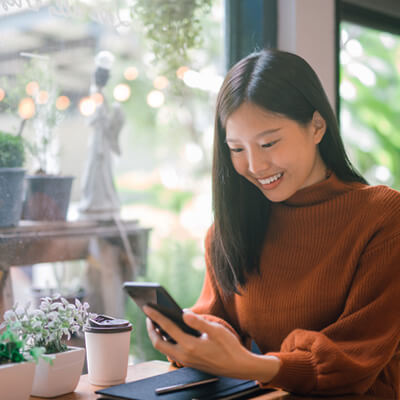 Person sitting in a café holding a smartphone beside a coffee cup and small potted plants.