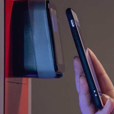 Hand holding smartphone near a contactless payment terminal on a vending machine.
