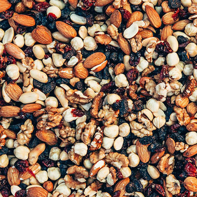 Close-up of a mix of nuts and dried fruits including almonds, walnuts, hazelnuts, and raisins, creating a colorful textured snack blend.
