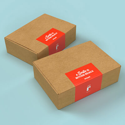 Two cardboard gift boxes with bright red labels on a light blue surface, featuring the message ‘A Smile Is Within Reach.