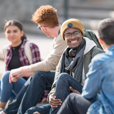 Group of students sitting outdoors on steps, talking and hanging out together.