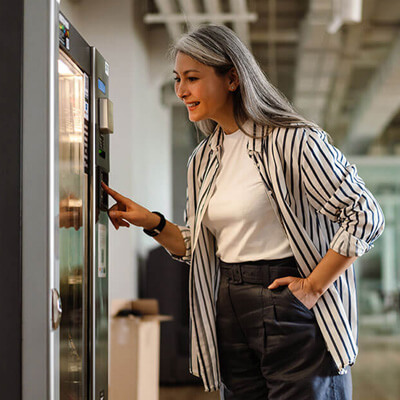 Person selecting an item from a vending machine in a modern office hallway.