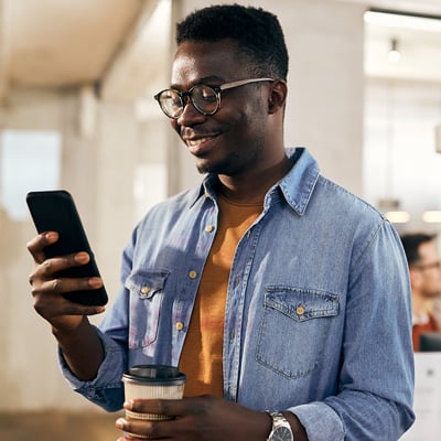 Person holding a smartphone and a coffee cup in a bright indoor setting.