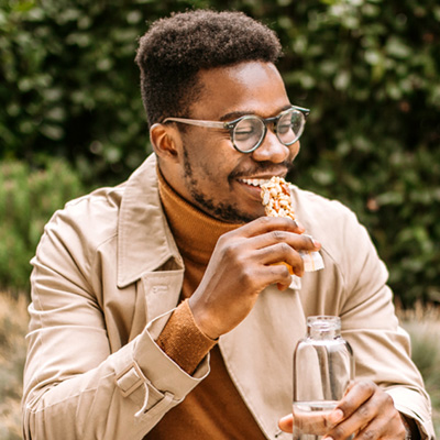 Person sitting outdoors holding a reusable water bottle surrounded by greenery.