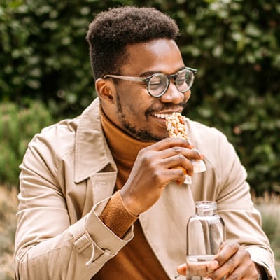 Person sitting outdoors holding a reusable water bottle surrounded by greenery.