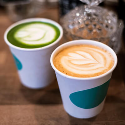 Two cups of latte art drinks, one green matcha and one coffee, on a wooden surface.