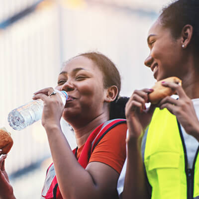 Workers in safety vests taking a break, drinking water and eating snacks outdoors.