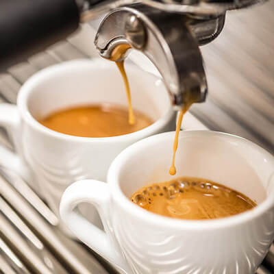 Close-up of two white ceramic cups being filled with freshly brewed espresso from a professional coffee machine.