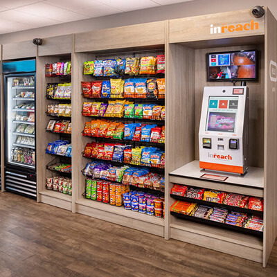 Self‑checkout micro market with refrigerated drinks, snacks, and a kiosk for purchasing items.