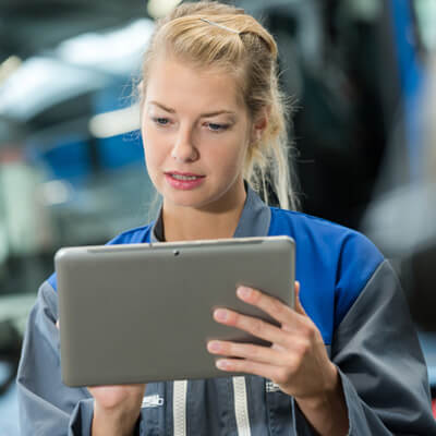 Worker in a blue uniform holding and using a tablet in an industrial setting.