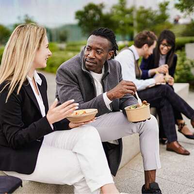 People sitting outdoors on steps sharing a casual meal together in a work or social setting.