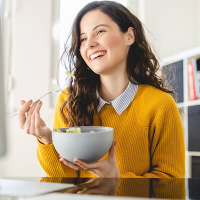 Person in a yellow sweater eating from a bowl at a table.