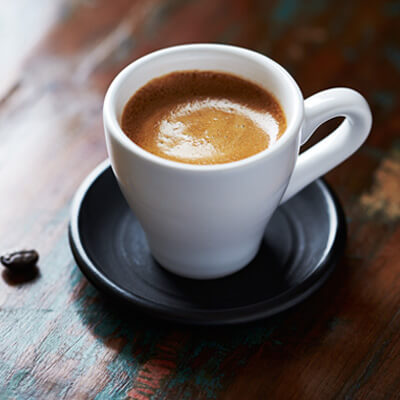 White cup of coffee on a black saucer resting on a rustic wooden table.