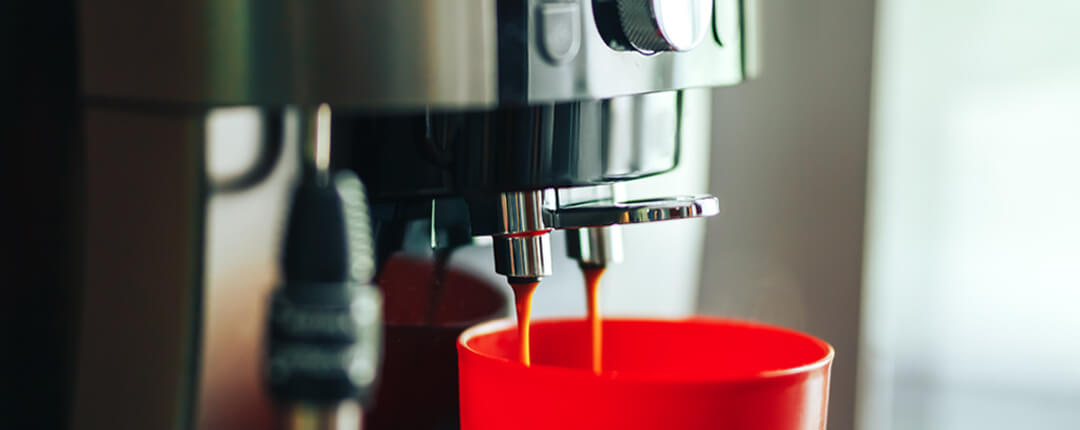 Close-up of an espresso machine pouring coffee into a bright red cup in a modern kitchen or café setting.