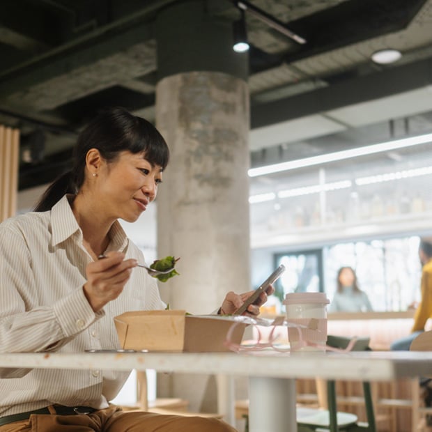 Woman looking at her phone while enjoying a meal in a break room.