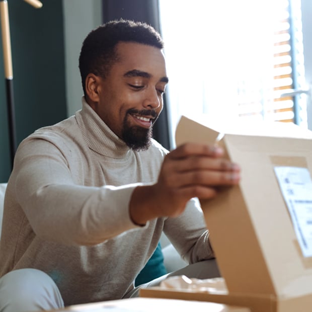Person opening a cardboard box while sitting indoors.