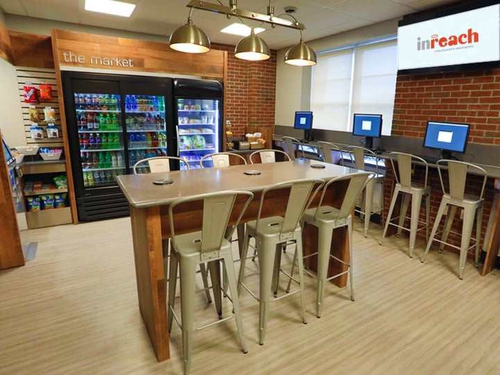 Cafeteria-style break area with drink coolers, a tall table with stools, and a row of computer kiosks.