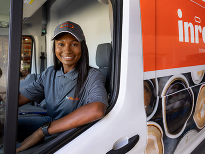 Person wearing an InReach uniform and cap seated inside a branded delivery vehicle.