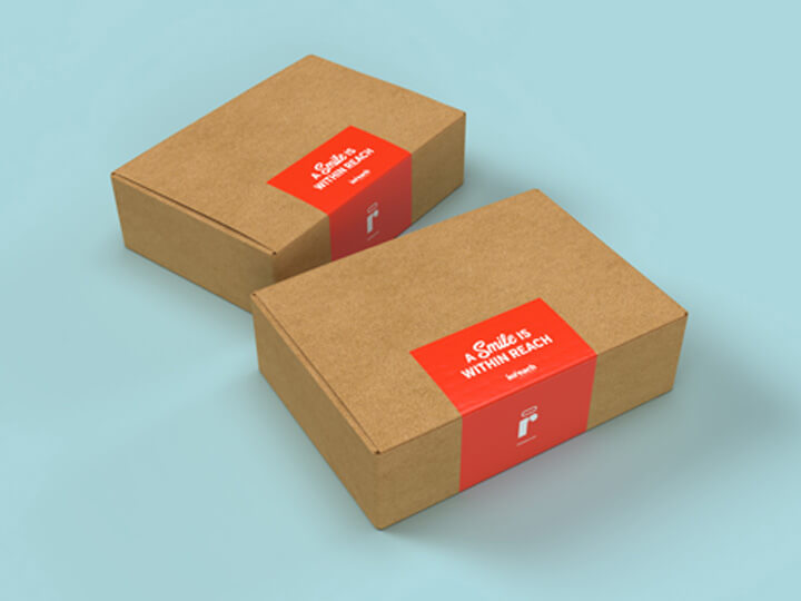 Two brown cardboard boxes with red labels reading “A Smile Is Within Reach” on a light blue surface.