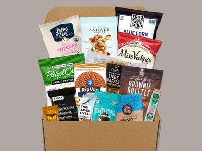 A box filled with assorted snacks including popcorn, chips, pretzels, cookies, nuts, and granola bars.