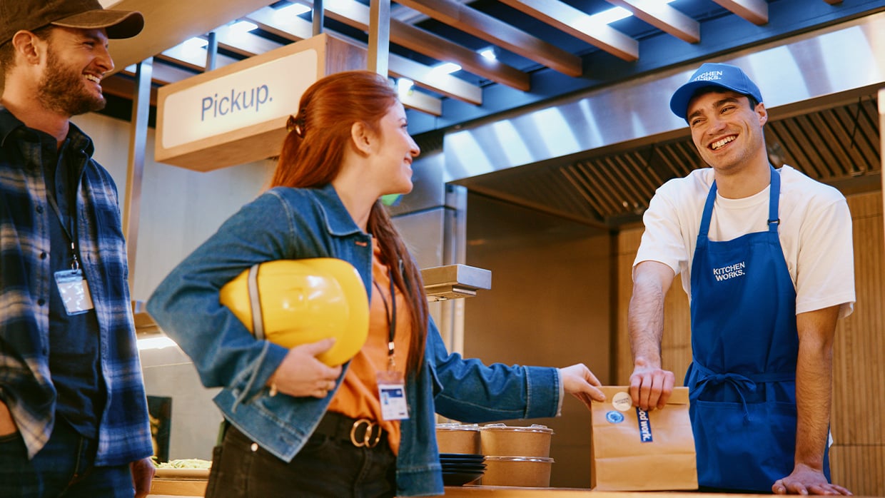 A man and woman stand together in front of a counter, engaged in conversation.