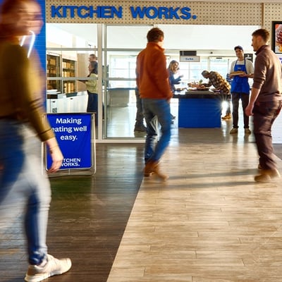 People outside a location called “KITCHEN WORKS” with a sign that says “Making eating well easy."