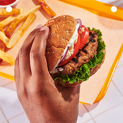 A hand holding a burger alongside a serving of fries on a tray