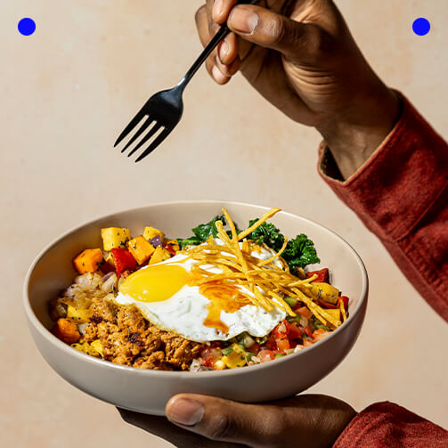 A person holds a fork above a bowl filled with food