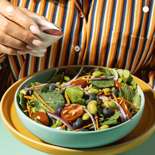 A woman holds a bowl of fresh salad in one hand and a fork in the other