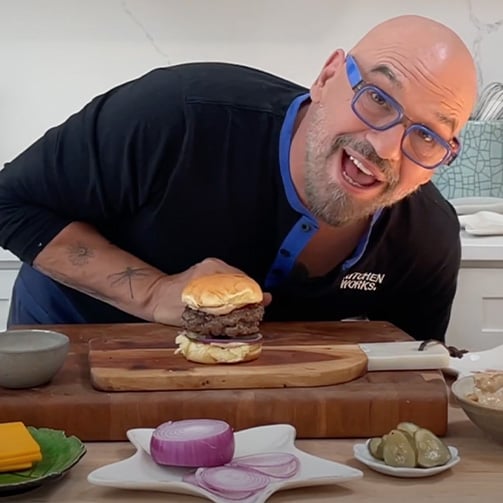 A man smiles while holding a large burger, showcasing his enjoyment of the meal.