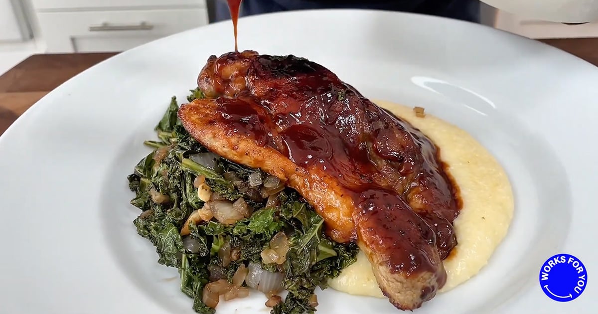 Close-up of a plate with slow-roasted pork butt steak with cherry BBQ sauce, creamy cheddar grits and balsamic collard greens.  