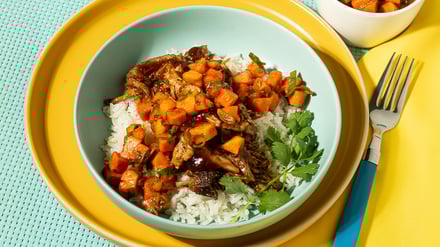 A plate of rice topped with seasoned meat, garnished with herbs, served on a white dish.