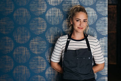 Chef Brooke Williamson posing in front of decorative wall