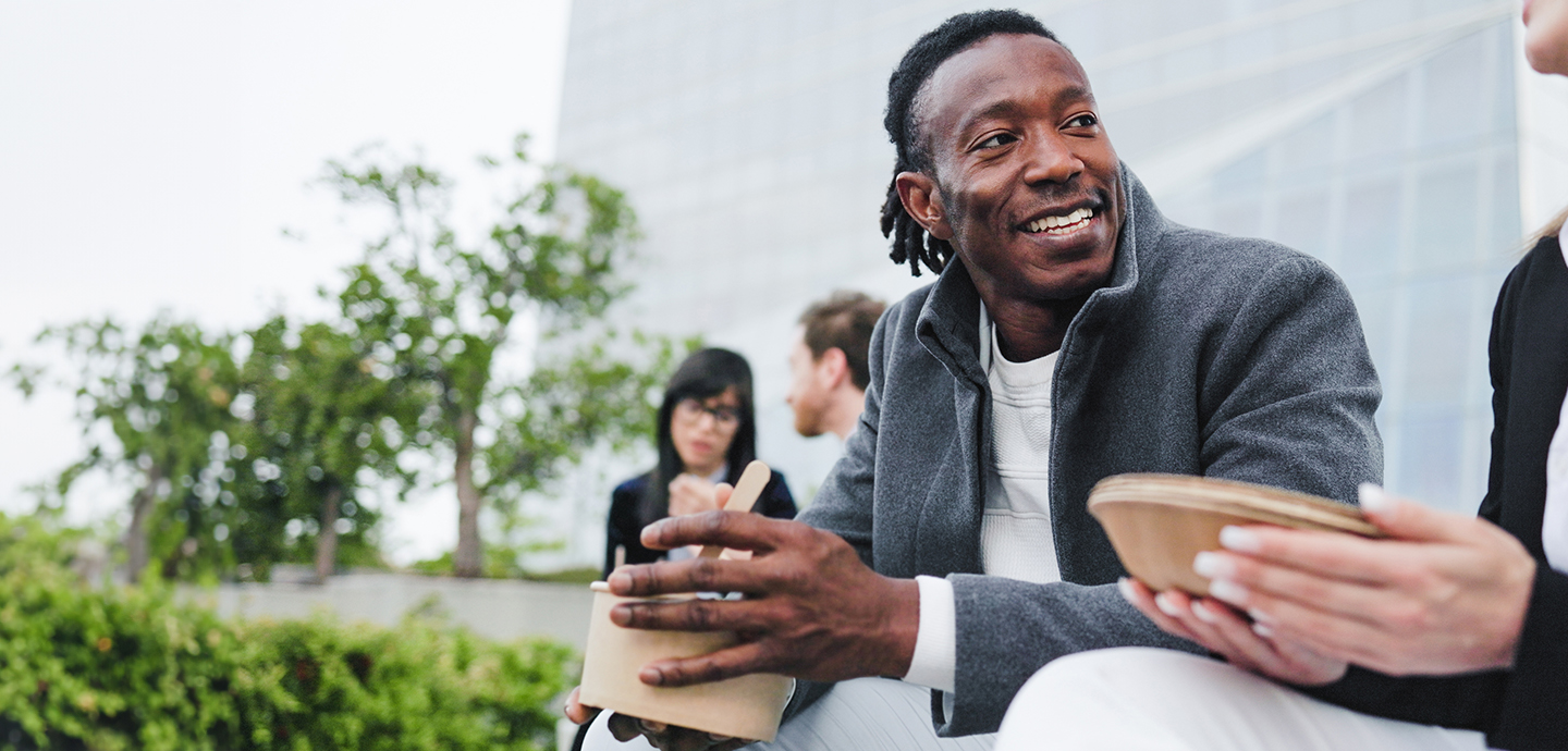 young black man eating outside and talking to a white person and smiling