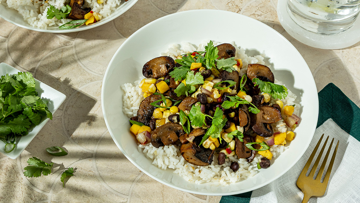 A bowl of rice topped with sautéed mushrooms and colorful mixed vegetables.