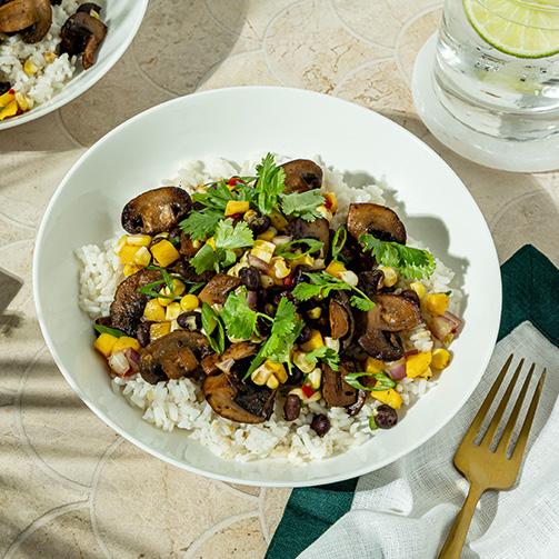 A bowl of rice topped with sautéed mushrooms and colorful mixed vegetables.