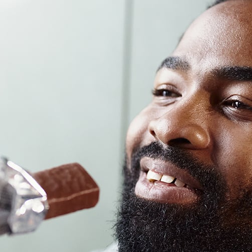 Close-up of a person with a beard being trimmed with an electric hair clipper, indoors with neutral-colored walls.