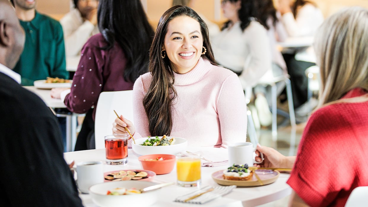 Group of people gathered around a table in a casual dining setting, enjoying a meal with a variety of dishes including waffles, fruit, and beverages