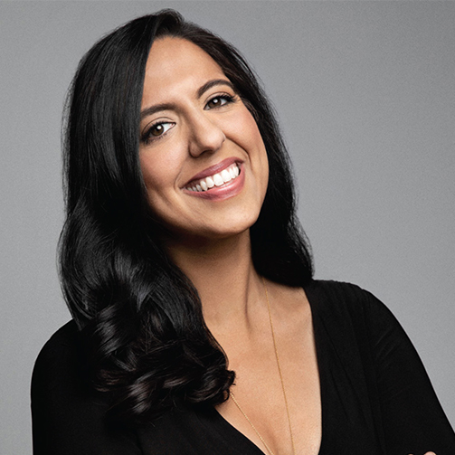 A woman with long hair smiles warmly at the camera, exuding a friendly and approachable demeanor.