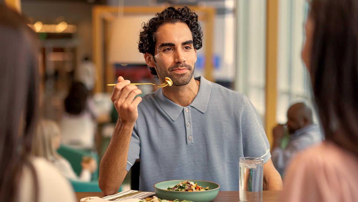 Man eating a meal at a restaurant table with two others, holding a fork over a bowl of food.
