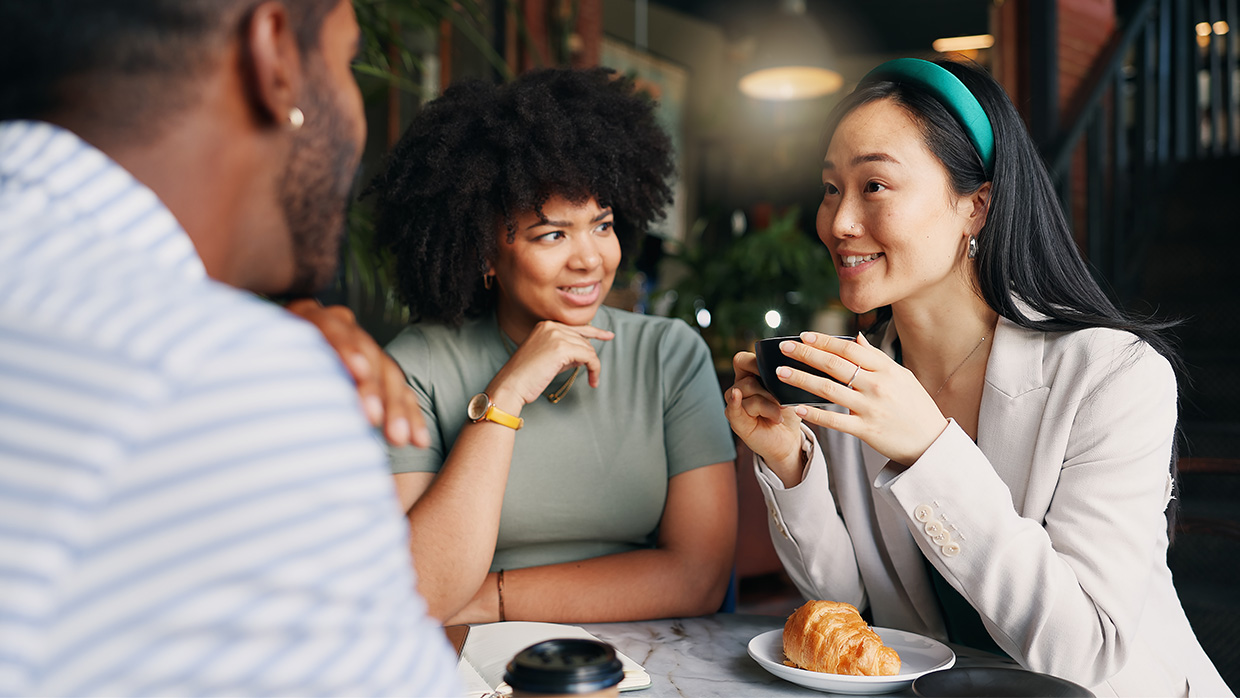 Three people seated at a table, enjoying coffee and engaged in conversation.