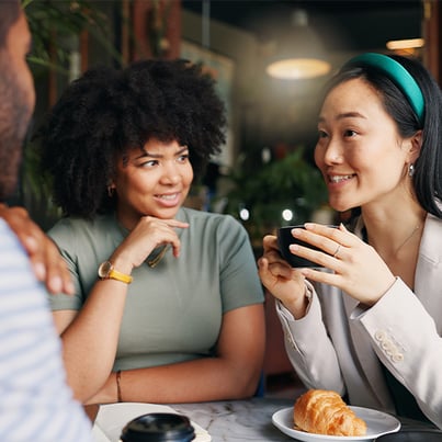 Three people seated at a table, enjoying coffee and engaged in conversation.